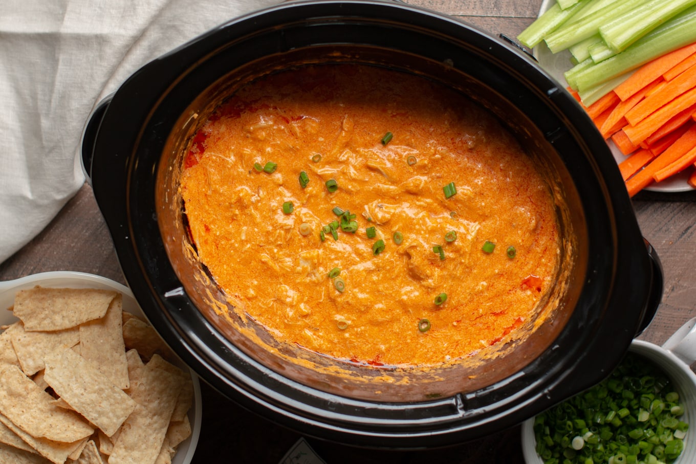 Cooked buffalo dip with corn chips and vegetables on the side.