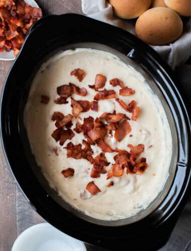 creamy potato soup in a slow cooker with bacon and rolls on the side.