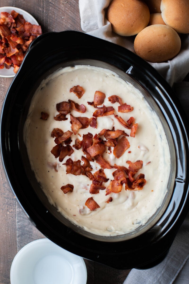 creamy potato soup in a slow cooker with bacon and rolls on the side.