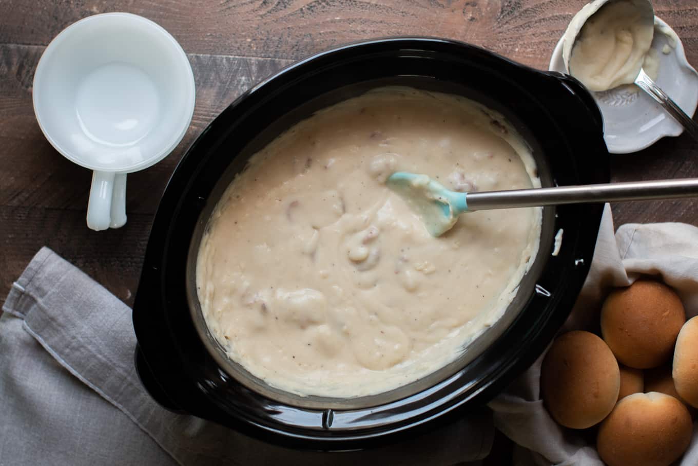 creamy blended potato soup in a slow cooker with bowls and rolls on the side.