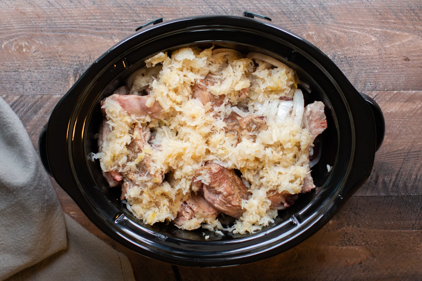 browned ribs, sauerkraut, potatoes, onion not yet cooked in a slow cooker.