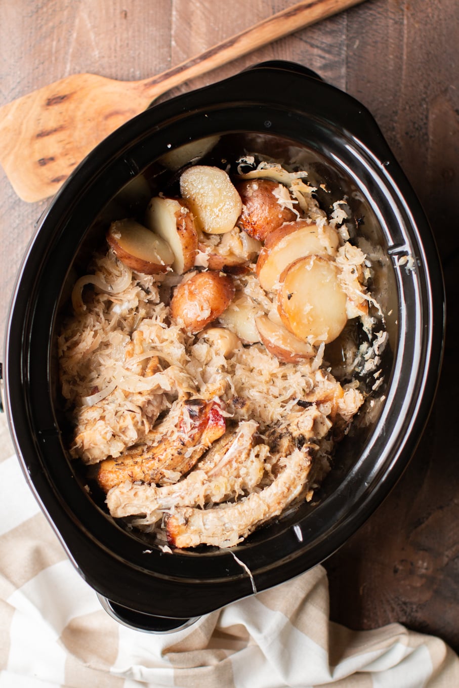 cooked ribs pieces in a slow cooker with potatoes and sauerkraut.