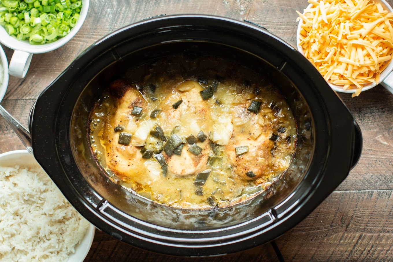 cooked chicken breasts with green chiles, onion and green enchilada sauce in a slow cooker.