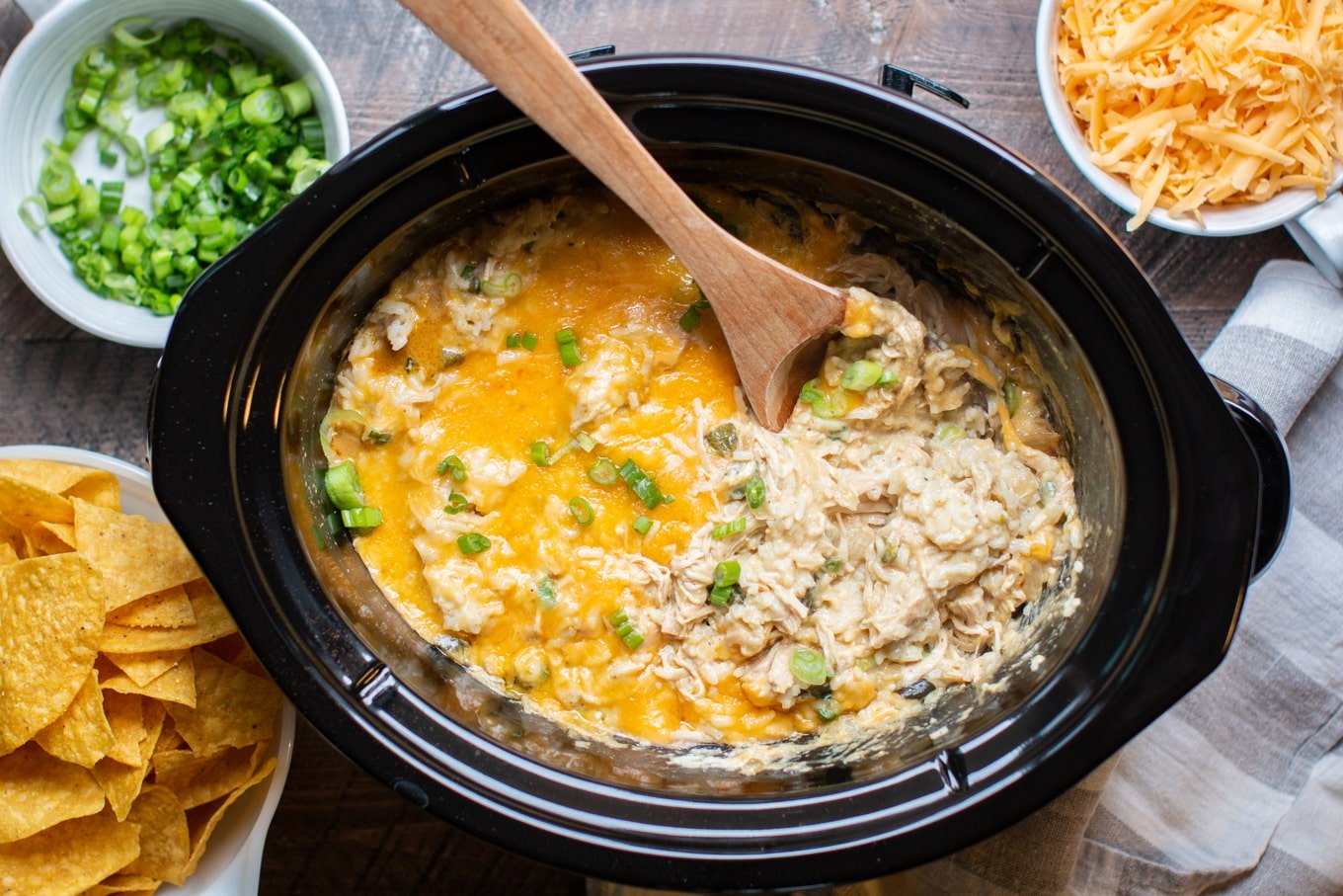 wooden spoon serving rice casserole with green chilies and chicken in a slow cooker.