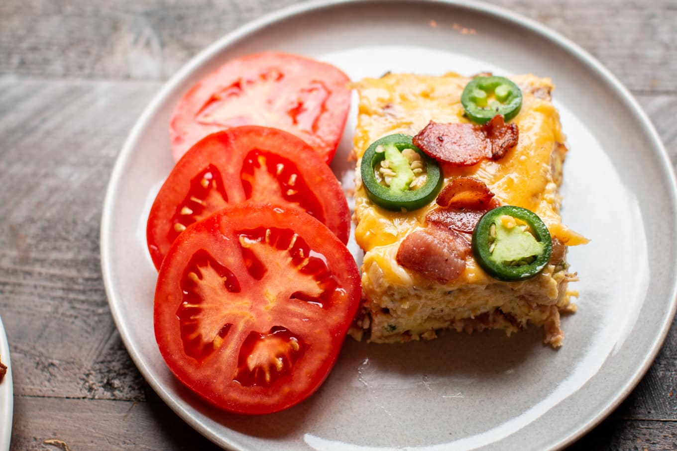 square or bacon jalapeno quiche with tomatoes on the side.