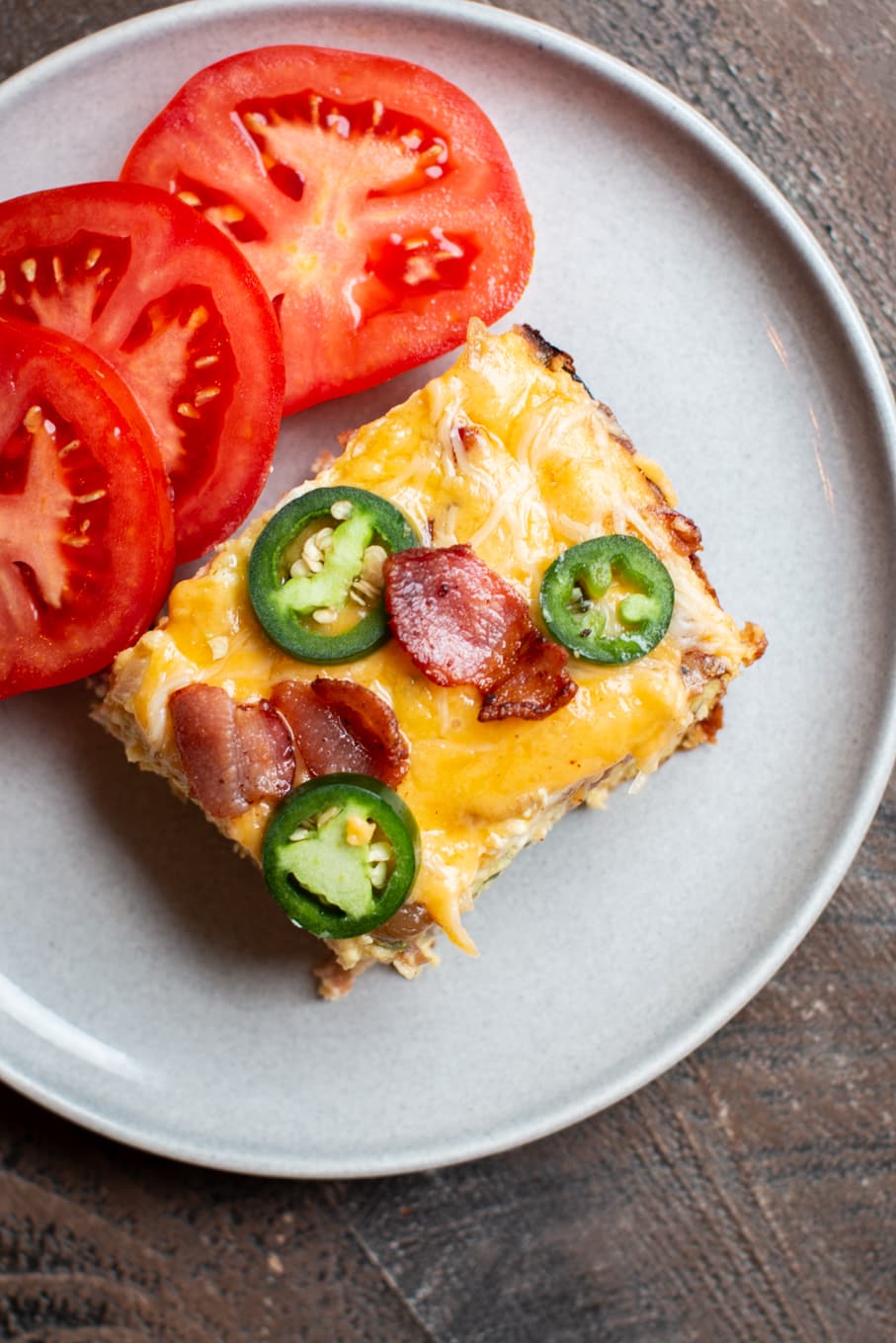slice of quiche with jalapeno and bacon on grey plate.