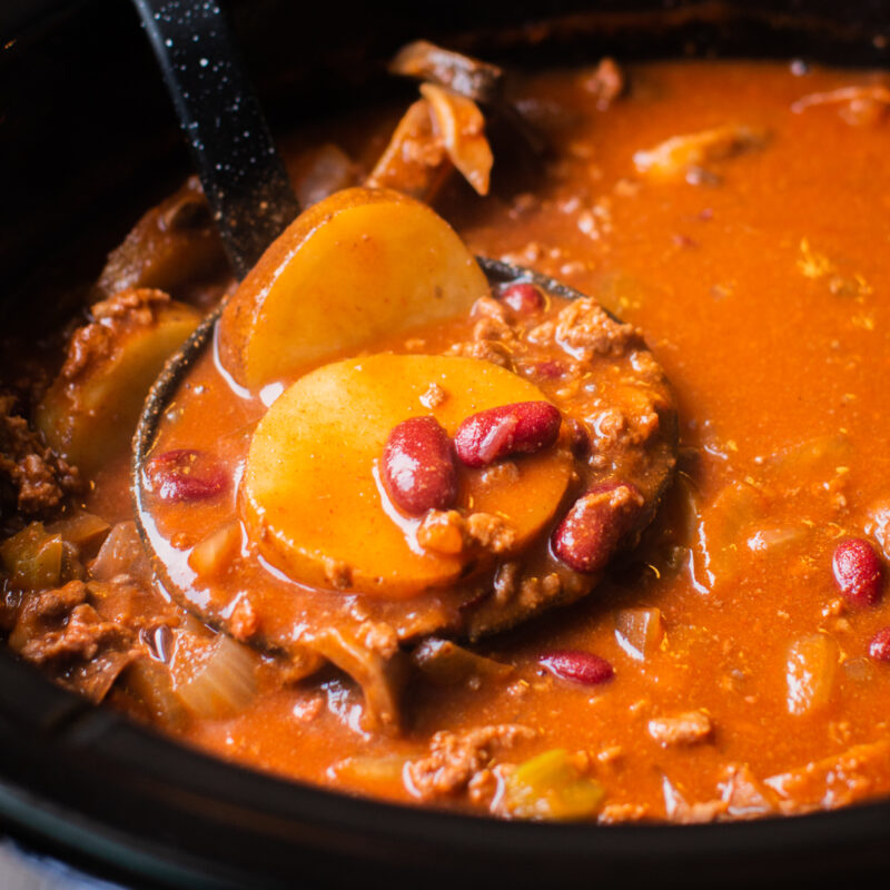 serving tomato-based stew with potatoes and kidney beans with a ladle