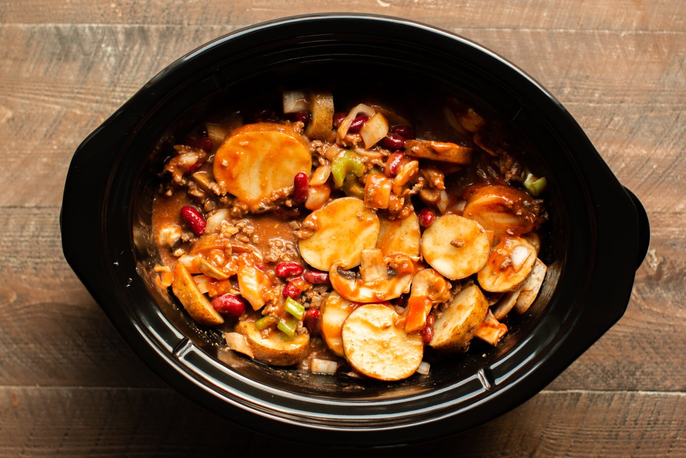 uncooked soup with potatoes, beef, celery and beans in a slow cooker.