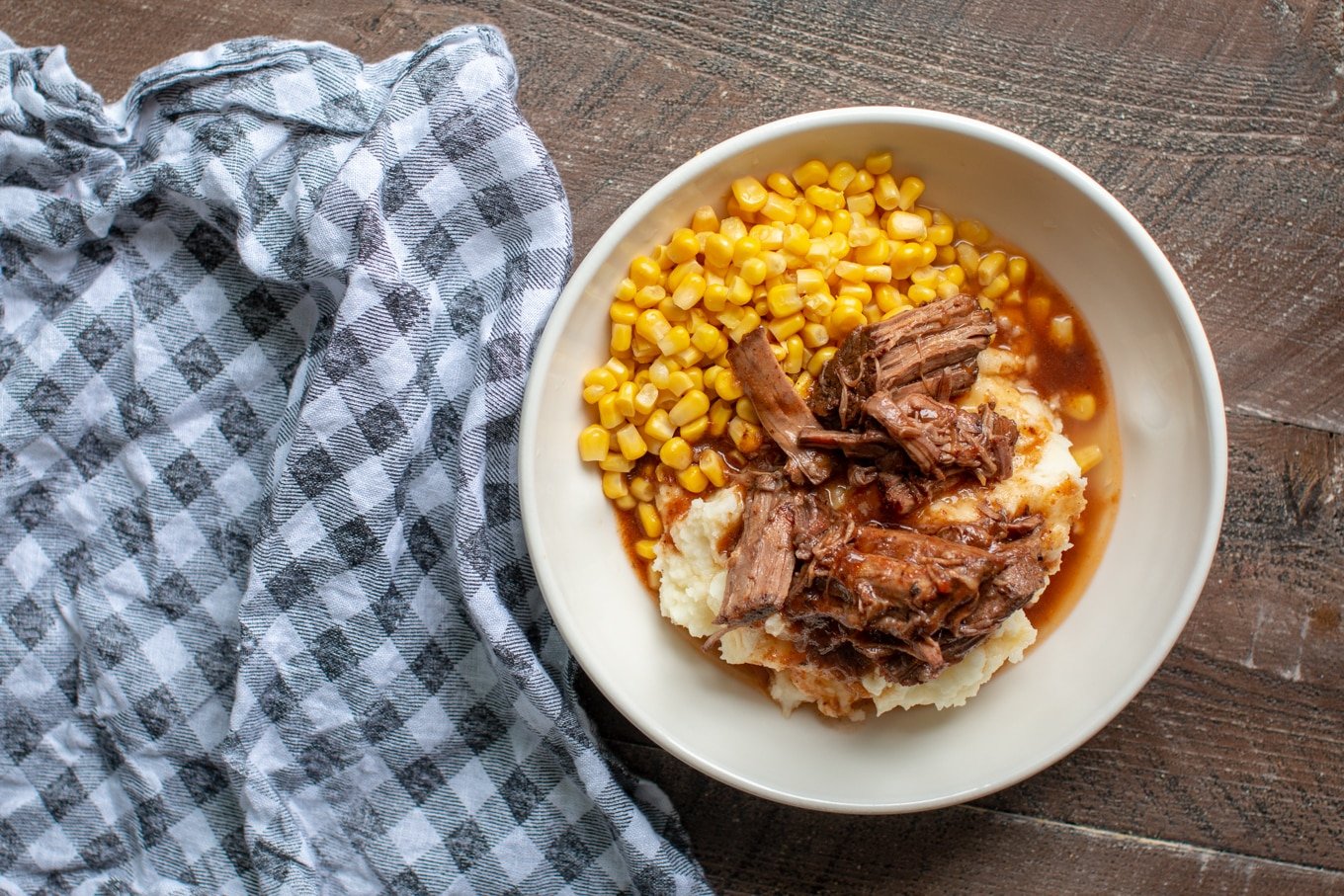 shredded beef and sauce on top of mashed potatoes with corn on the side.