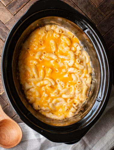 Mac and cheese cooked in a slow cooker with wooden spoon on the side.