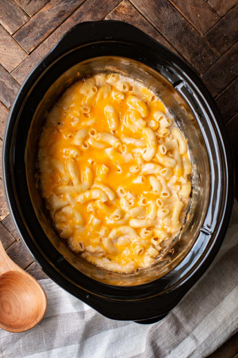 Mac and cheese cooked in a slow cooker with wooden spoon on the side.