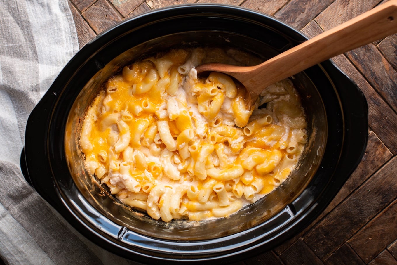 Cooked large macaroni and cheese in the slow cooker, large wooden spoon in it.
