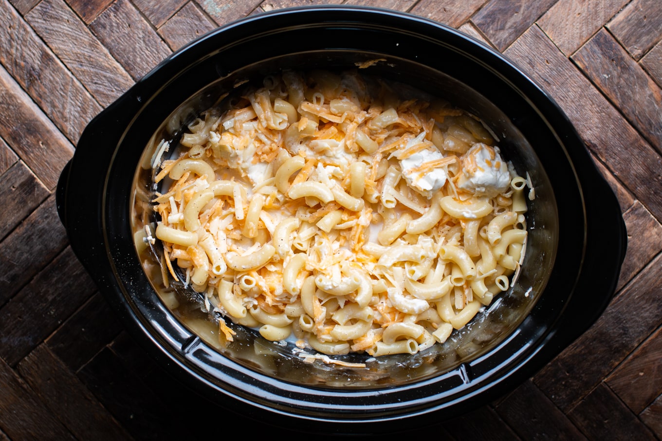 Cooked macaroni noodles, cream cheese and cheddar cheese before cooked in a slow cooker.