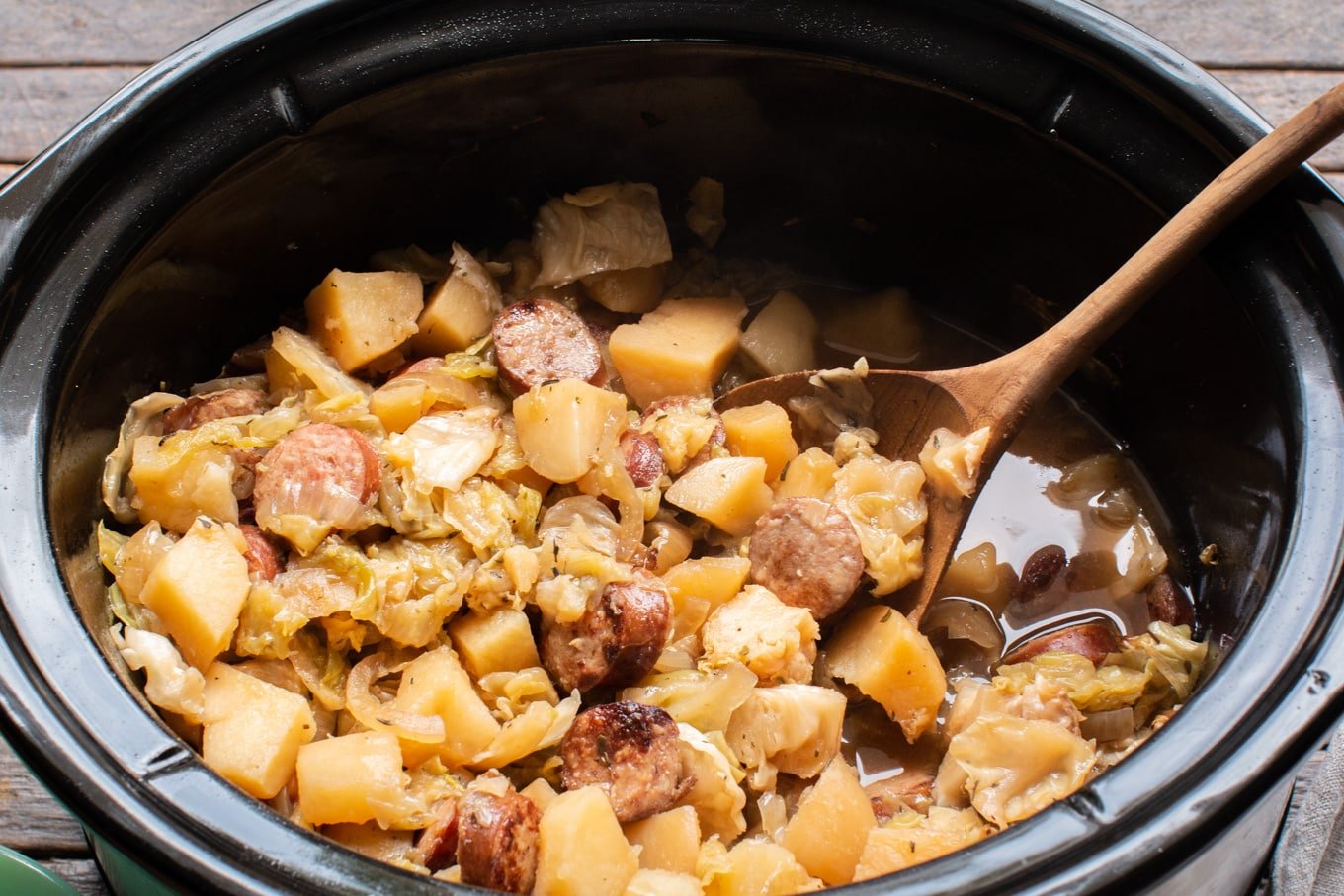 close up of potato, kielbasa, cabbage meal with a wooden spoon in it.