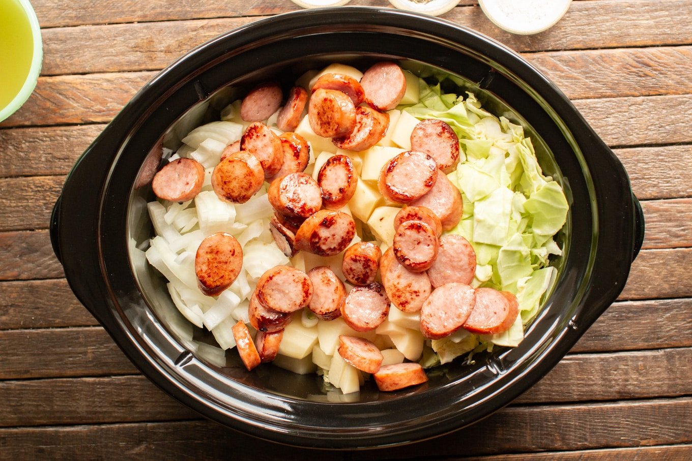 uncooked onion, potatoes, and browned kielbasa in a slow cooker.