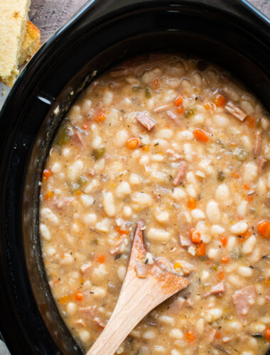 close up photo of white beans and ham with wooden spoon in them.