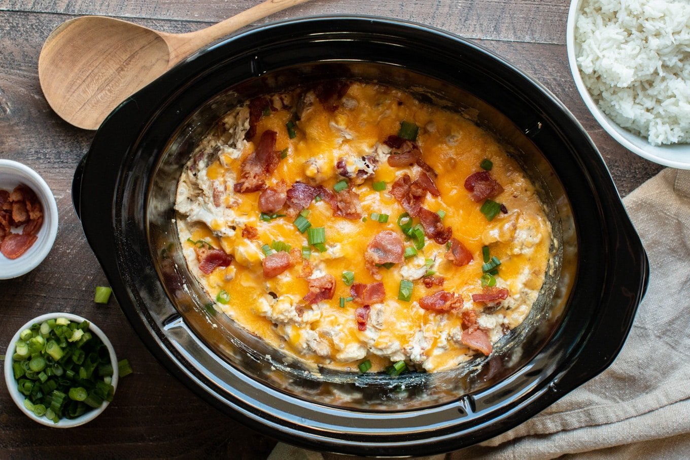 Finished crack chicken in slow cooker with bacon, cheese and green onion on top.