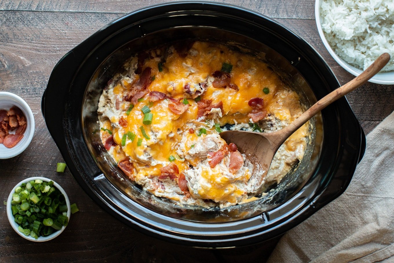 shredded creamy chicken with cheese, bacon and green onion on top, in the slow cooker.