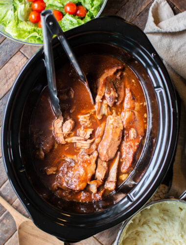 Tongs in sweet and sour ribs in the slow cooker.