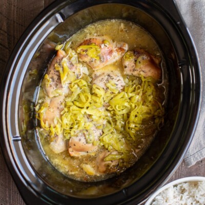 chicken in the slow cooker with sauce and pepperoncini peppers on top.