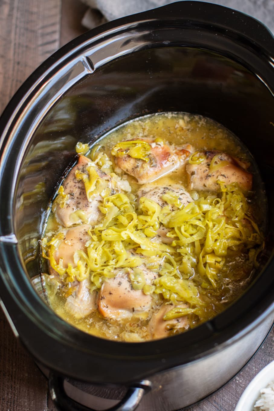 cooked chicken thighs in the slow cooker with pepperoncinis on top.