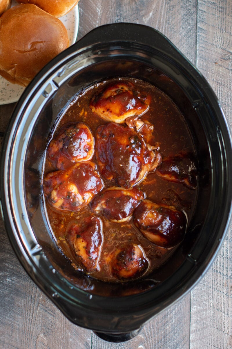 Nine chicken thighs in slow cooker in a root beer barbecue sauce.