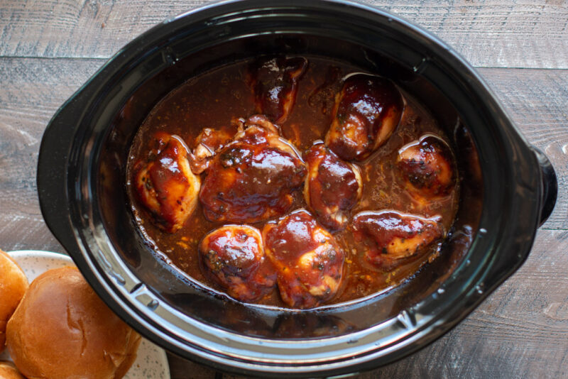 Barbecue chicken thighs in slow cooker with buns on the side.