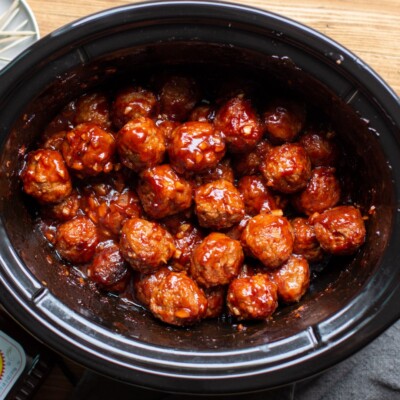 Slow cooker half full with meatballs, barbecue sauce and onions.