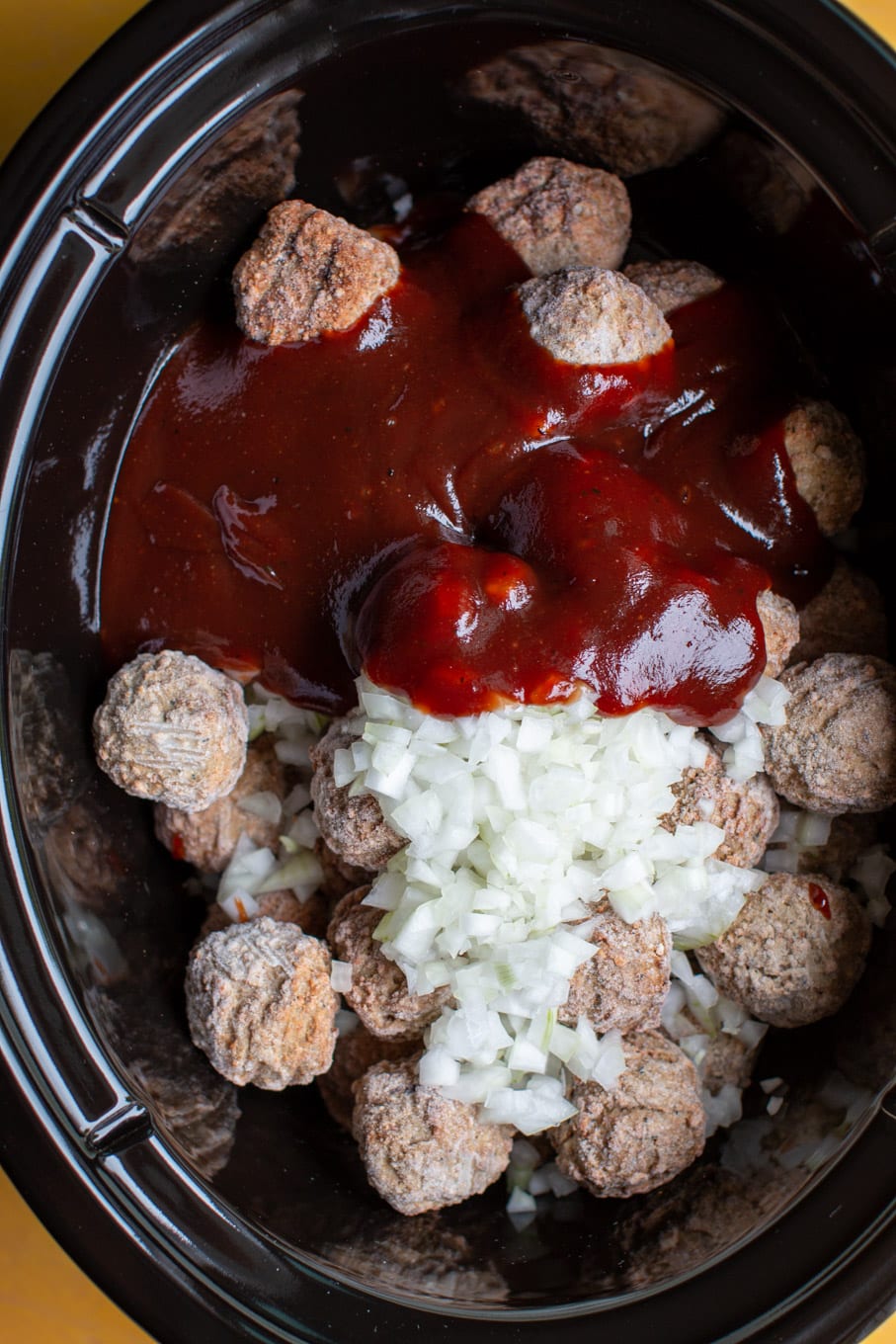 meatballs in a slow cooker with barbecue sauce poured over and diced onion.