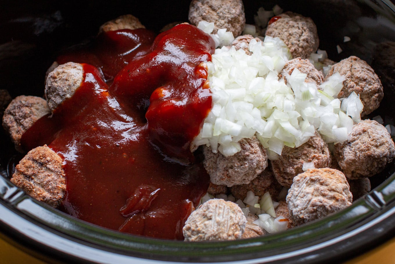 frozen meatballs with barbecue sauce and onions on top in a slow cooker.