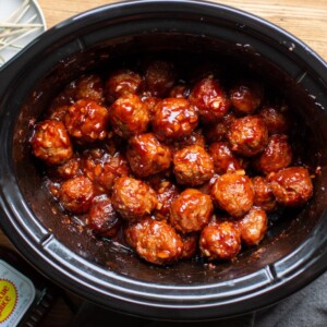 meatballs in a slow cooker with bottle of barbecue sauce and toothpicks on the side.