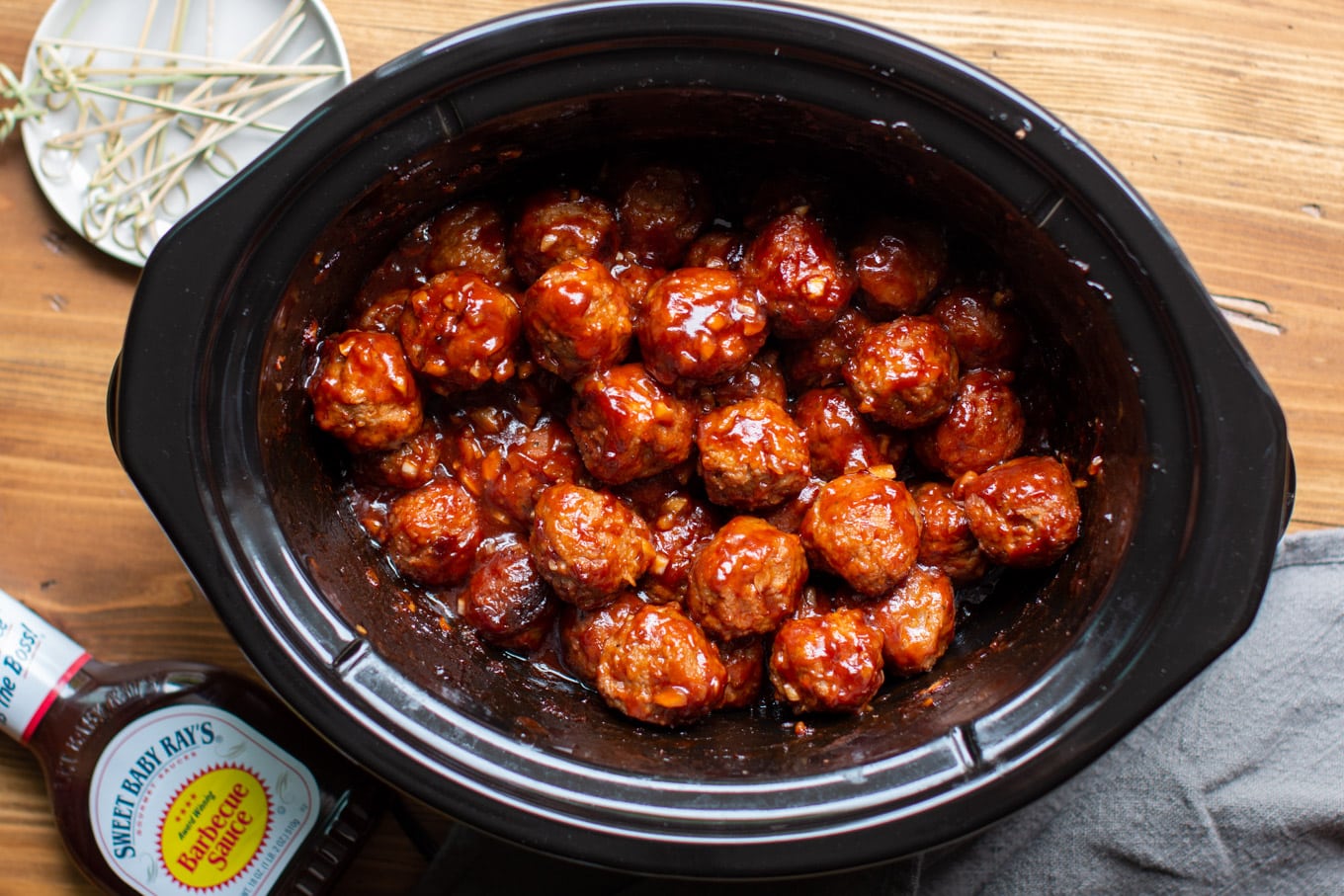 meatballs in a slow cooker with bottle of barbecue sauce and toothpicks on the side.