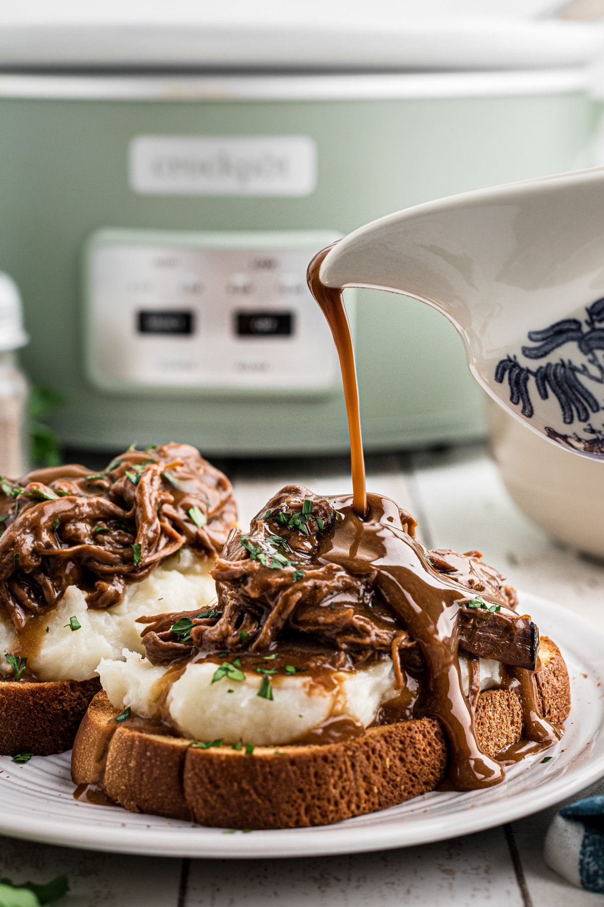 Gravy being poured over roast beef, mashed potatoes and toast.