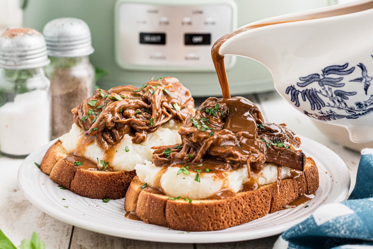 Gravy being pour over a hot roast beef sandwich.