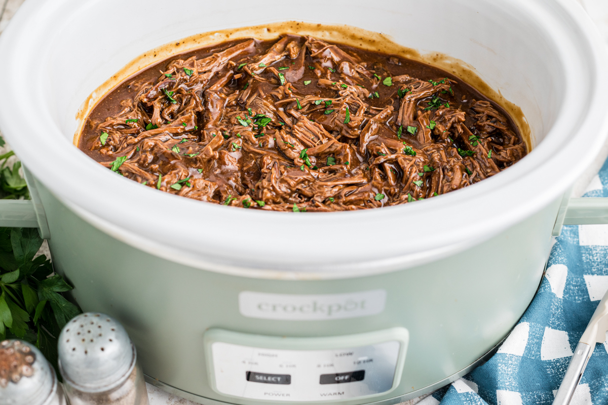 shredded roast beef in gravy in a slow cooker.