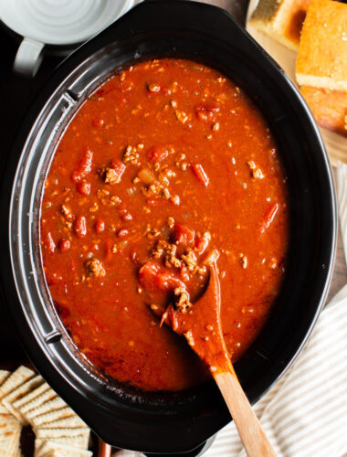 v8 chili in a slow cooker with a wooden spoon in it.