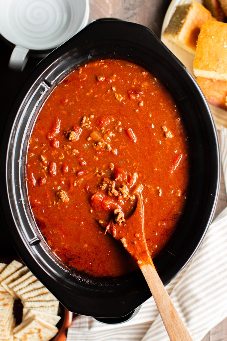 v8 chili in an oval slow cooker with cornbread on the side.