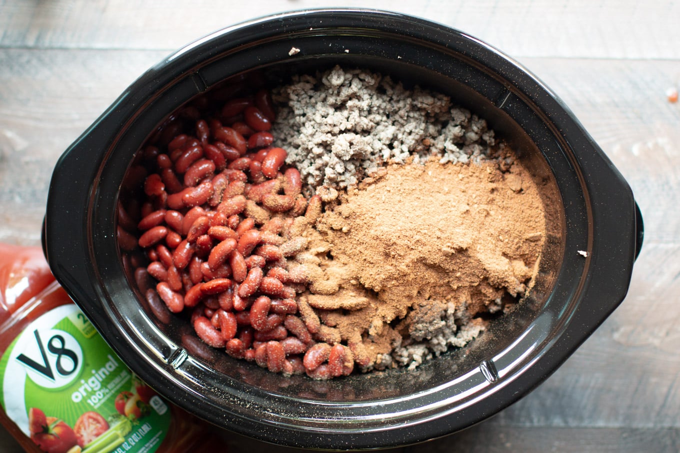 Kidney beans, ground beef and chili seasoning in separate piles in a slow cooker.