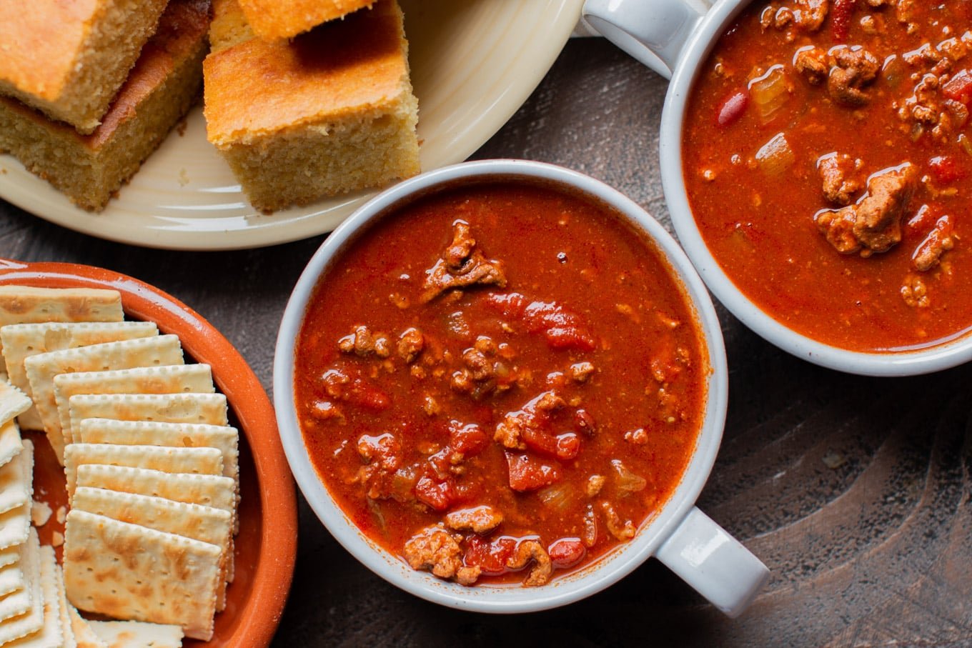 2 bowls of chili with crackers and cornbread on the side.