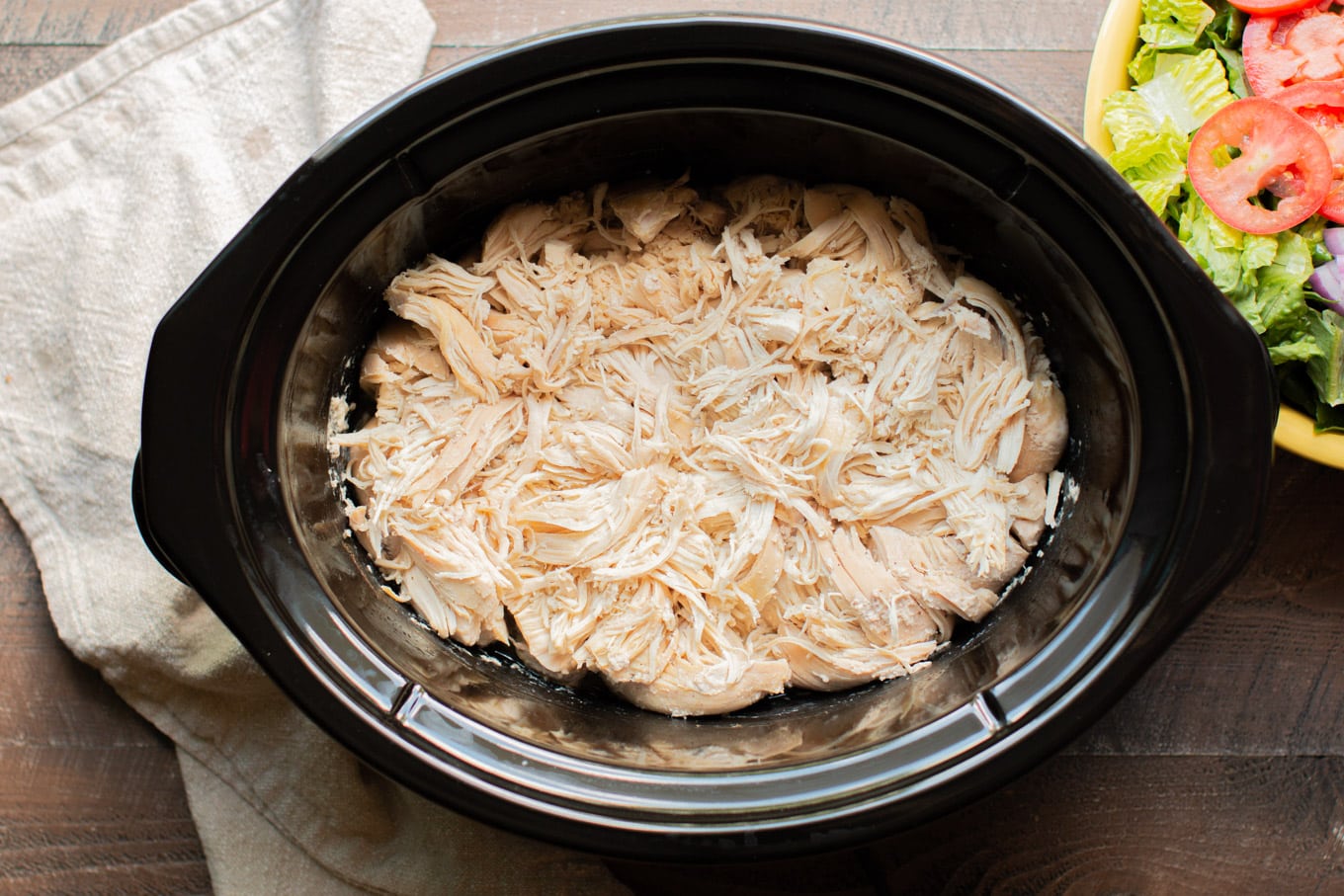 Slow cooker half full of white meat shredded chicken.