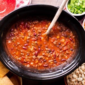 Finished cooking venison chili in a slow cooker with a wooden spoon in it.