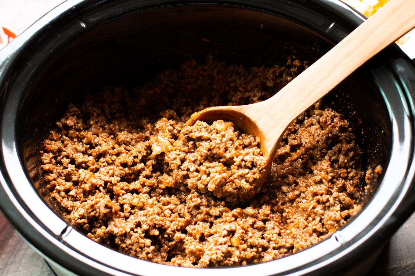 serving hot dog chili with a wooden spoon from an oval slow cooker.