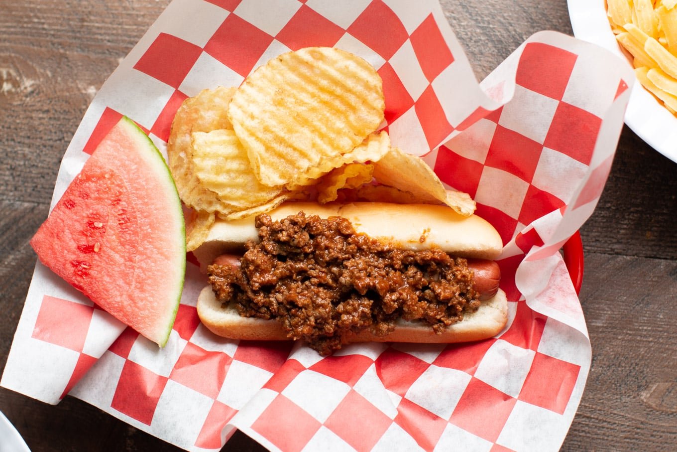 hot dog with chili on top on red and white checkered paper