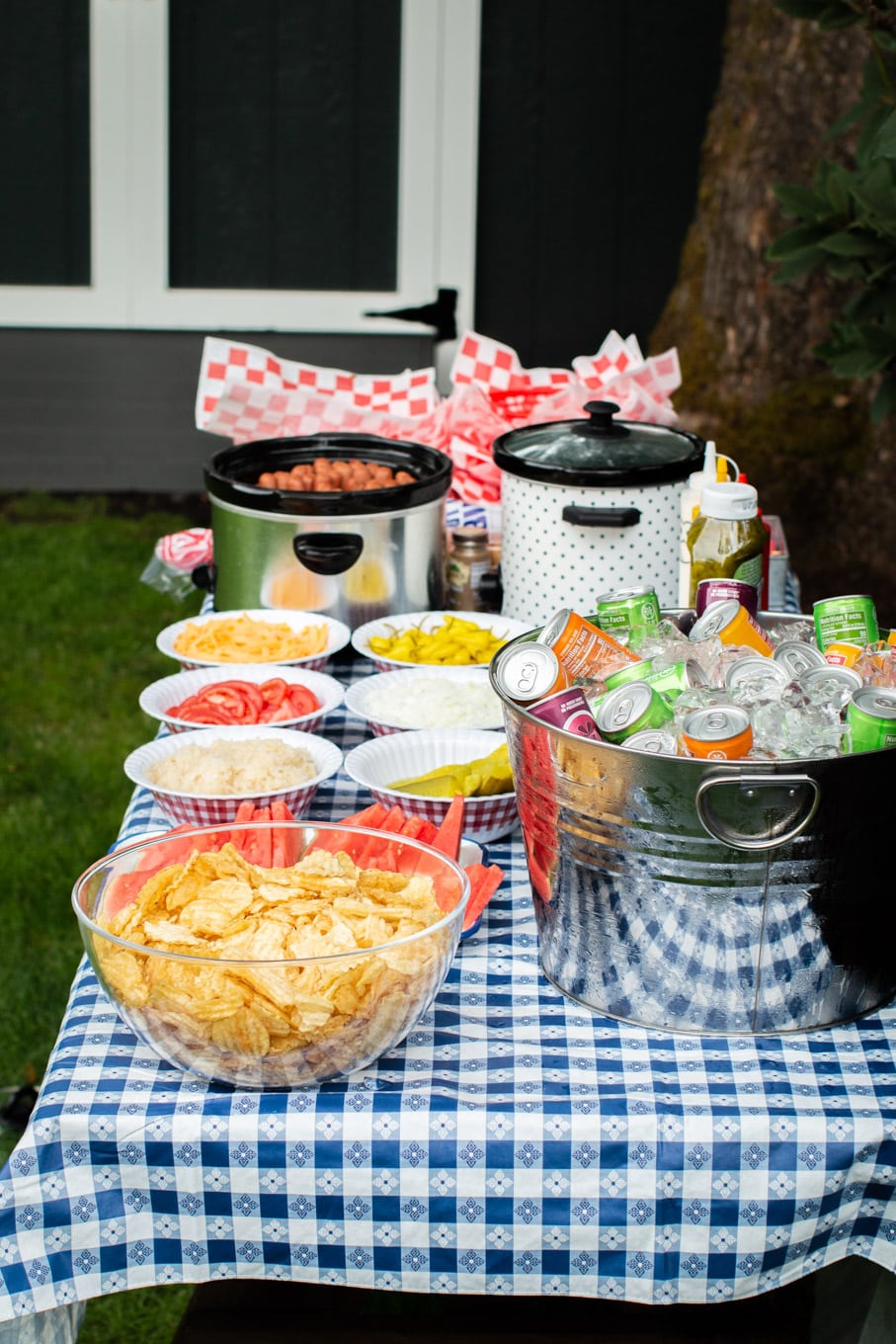 Side view of a hot dog bar with chips and drink bucket.