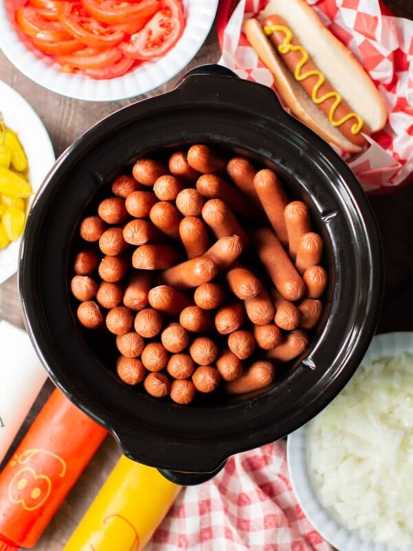 slow cooker full of hot dogs with condiments on the side.