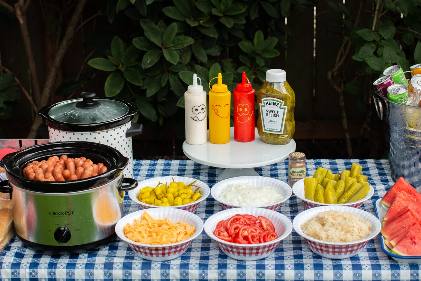 hotdog bar with slow cookers, bowls of peppers, cheese, tomatoes, sauerkraut, pickles and onions.