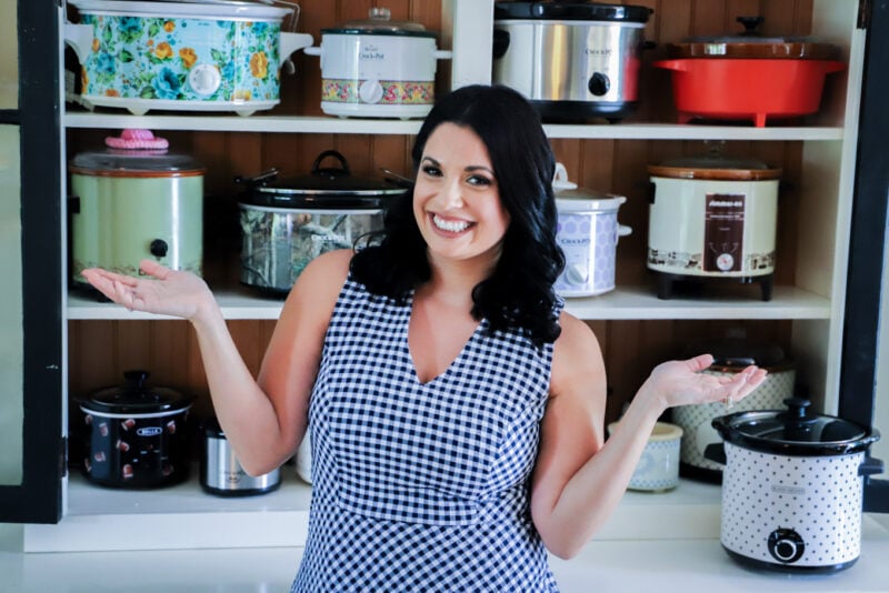 A woman with her arms up in front of shelves full of slow cookers.