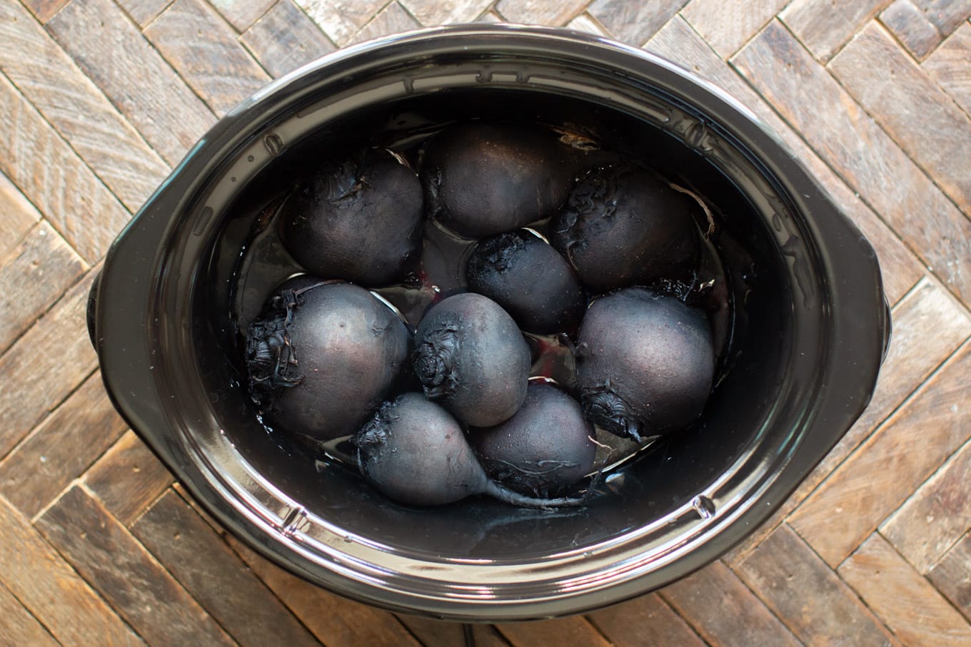 dark colored cooked beets with skins still on, in a slow cooker.