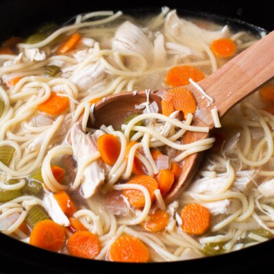 close up of chicken noodle soup with wooden ladle in it.