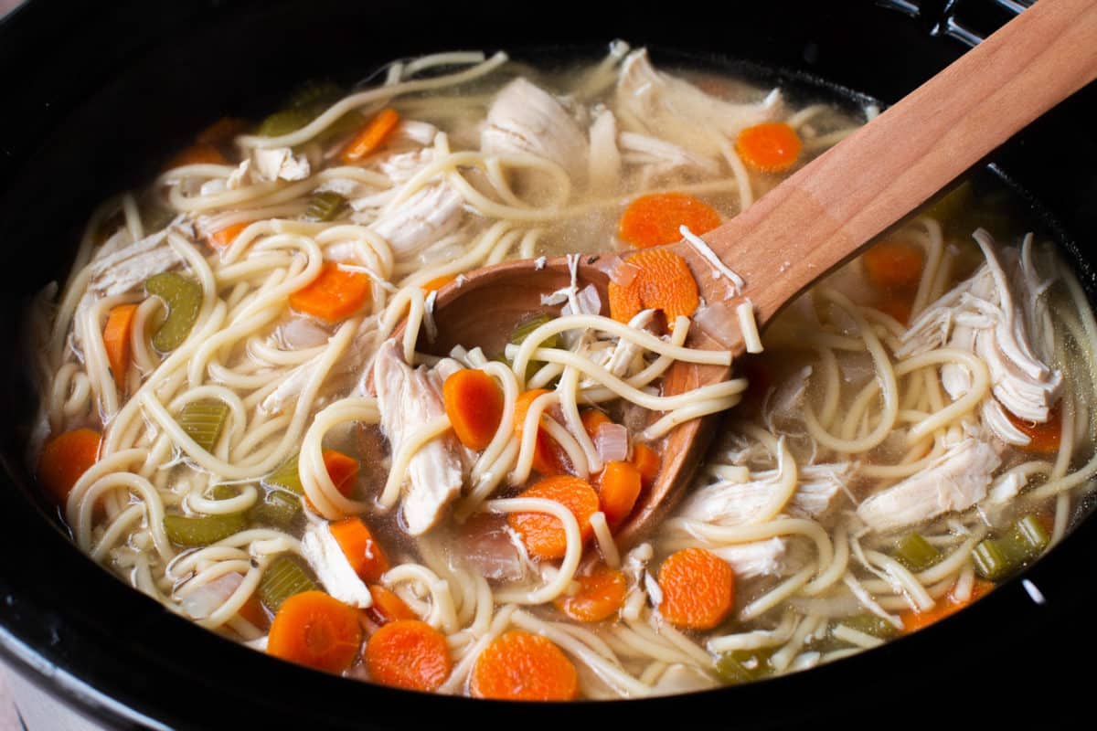 close up of cooked chicken noodle soup in a slow cooker.